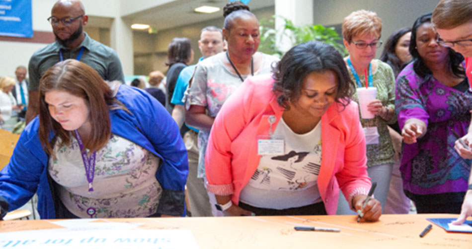 Employees signing a large pledge banner and filling out a personal pledge card to put up in their workspaces