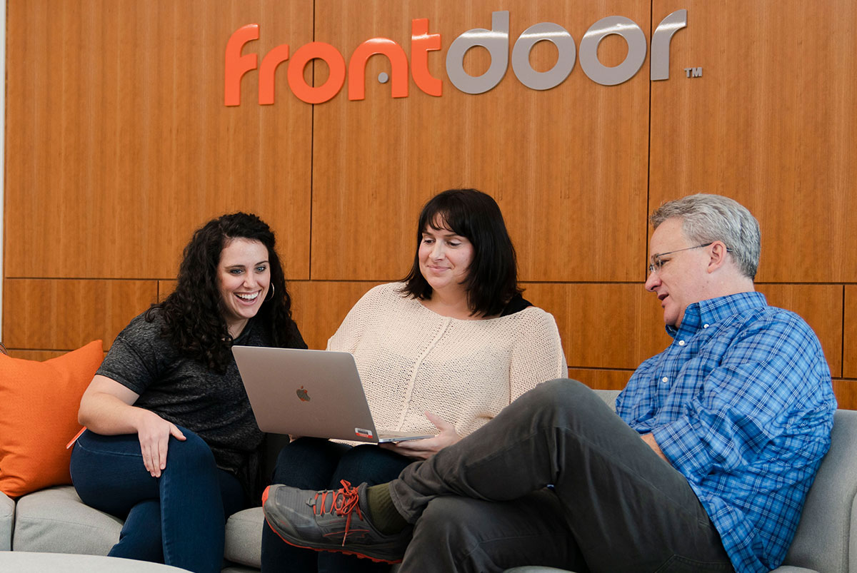 Life at Frontdoor. 2 women and 1 man looking at a laptop while sitting on a couch at Frontdoor