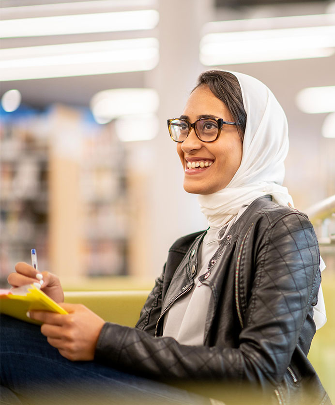 Young woman wearing head scarf smiling and taking notes in a meeting